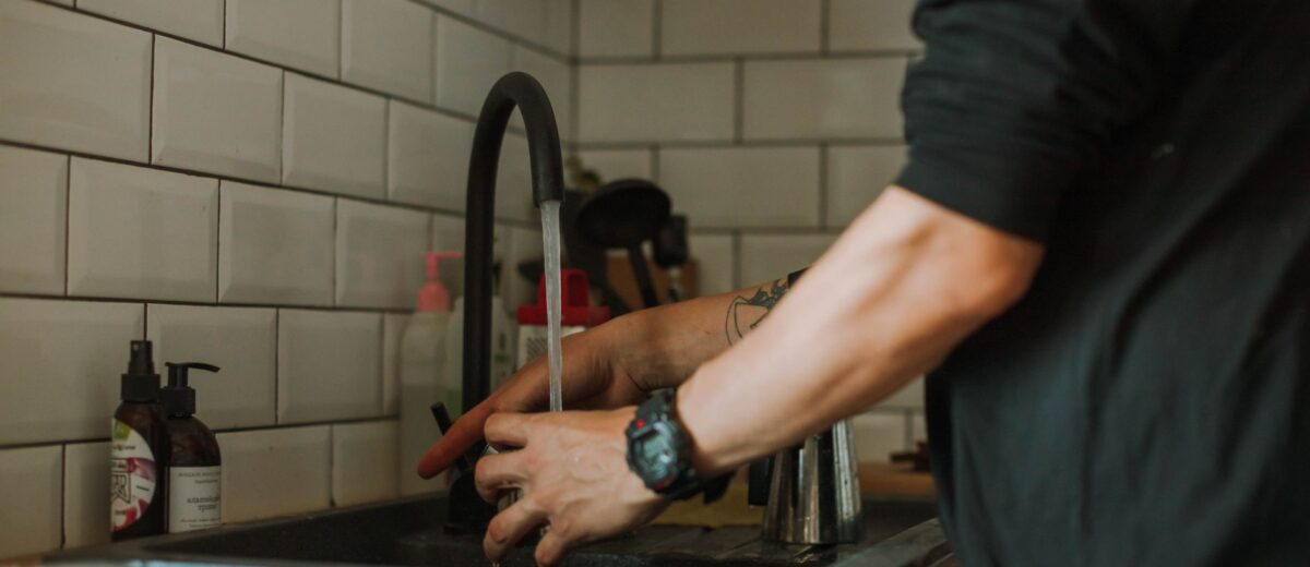 Close-up of a person washing hands at a sink with running water, wearing a wristwatch.