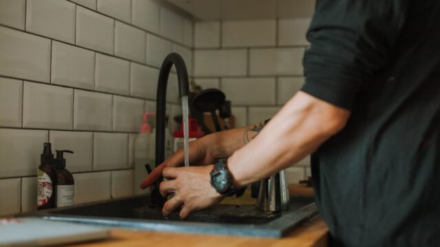 Close-up of a person washing hands at a sink with running water, wearing a wristwatch.