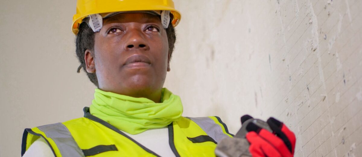 Portrait of a female construction worker in safety gear holding a wrench indoors.