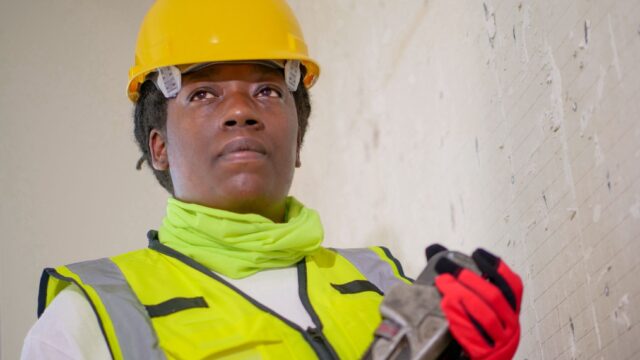 Portrait of a female construction worker in safety gear holding a wrench indoors.