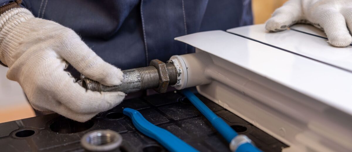 Close-up of a plumber installing a radiator pipe using specialized tools.