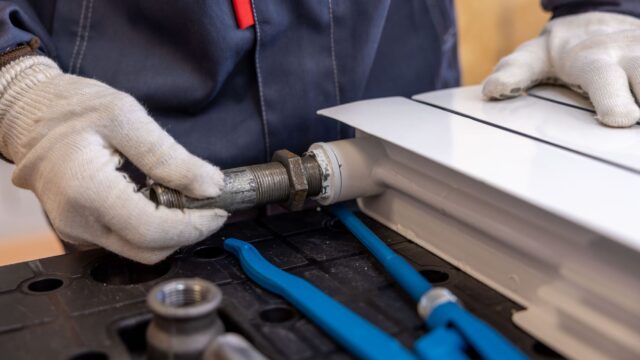 Close-up of a plumber installing a radiator pipe using specialized tools.