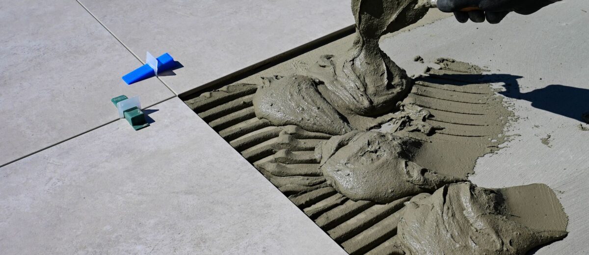 Close-up of a gloved hand applying mortar for ceramic tile installation outdoors.
