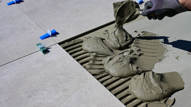 Close-up of a gloved hand applying mortar for ceramic tile installation outdoors.