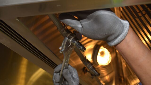 A worker fixing pipes with tools in an industrial indoor environment.