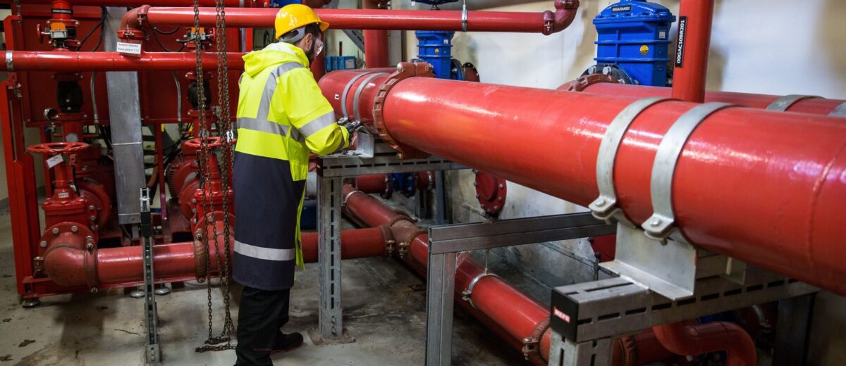 Engineer with safety gear inspecting red industrial piping system indoors.