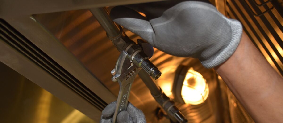 A worker fixing pipes with tools in an industrial indoor environment.